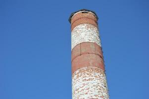 Round industrial red and white brick pipe against a blue sky. photo
