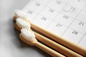 On a light gray background, there is a calendar with a dentist's note and toothbrushes. photo