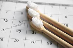 On a light gray background, there is a calendar with a dentist's note and toothbrushes. photo