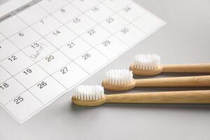 On a light gray background, there is a calendar with a dentist's note and toothbrushes. photo