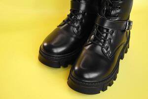 Black high leather boot on a yellow background. photo