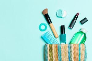 productos de maquillaje que se derraman de la bolsa de cosméticos sobre fondo azul pastel con espacio vacío para su diseño foto