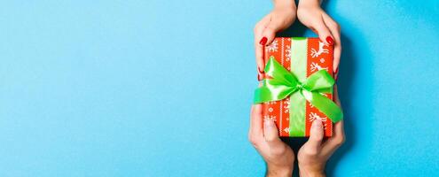 Top view of two people sharing a present on colorful background. Holiday and surprise concept. Close up photo