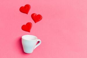 fiesta composición de rojo corazones que cae fuera desde un taza en vistoso antecedentes. parte superior ver de Santo San Valentín día concepto con Copiar espacio foto