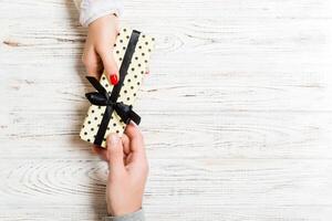 Top view of male and female hands holding present box on wooden background. Sharing a gift concept. Copy space photo