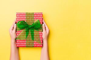 Woman arms holding gift box with colored ribbon on yellow table background, top view and copy space for you design photo