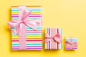 Gift box with pink bow for Christmas or New Year day on yellow background, top view photo