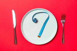 Question mark made of measuring tape on round plate on red background. Top view of hesitation and diet concept photo