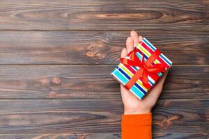 Top view of female hands holding christmas or other holiday handmade present box package in the palms, flat lay on dark table background with copy space photo