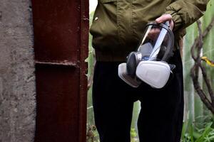 A man holds a respirator against the backdrop of the entrance of a home bomb shelter. photo