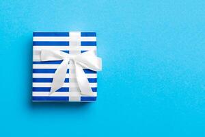 Gift box with white bow for Christmas or New Year day on blue background, top view with copy space photo