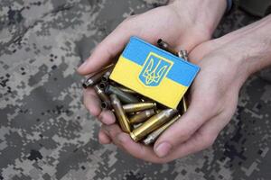 Dirty male hands hold a bunch of shell casings with the Ukrainian flag on top. photo