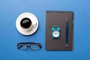 Modern office desk table with notebook and other supplies with cup of coffee. Blank notebook page for you design. Top view, flat lay photo