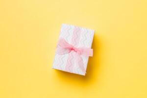 Gift box with pink bow for Christmas or New Year day on yellow background, top view with copy space photo