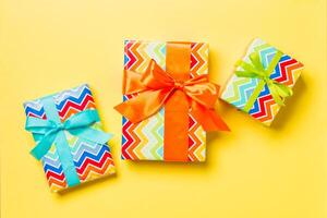 Gift box with blue, green and orange bow for Christmas or New Year day on yellow background, top view photo