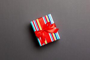 wrapped Christmas or other holiday handmade present in paper with red ribbon on black background. Present box, decoration of gift on colored table, top view with copy space photo