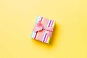 wrapped Christmas or other holiday handmade present in paper with pink ribbon on yellow background. Present box, decoration of gift on colored table, top view with copy space photo