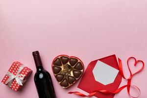 Bottle of red wine on colored background for Valentine Day with gift box, envelope and chocolate. Heart shaped with gift box of chocolates top view with copy space photo