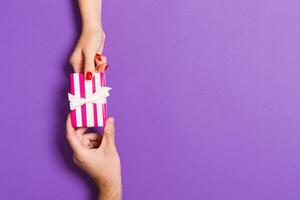 Top view of giving and receiving a present on colorful background. A man and a woman holding gift in hands. Festive concept with copy space photo