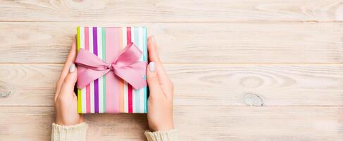 Girl Hands holding craft paper gift box with as a present for Christmas or other holiday on yellow rustic wooden background, top view with copy sppace photo