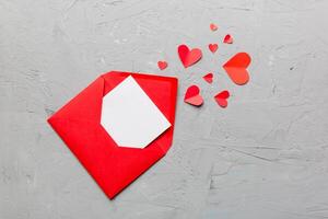 Red paper envelope with empty white card and heart on colored background. top view valentines day concept photo
