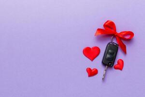 Car key with a red bow and a heart on Colored table. Giving present or gift for valentine day or christmas, Top view with copy space photo