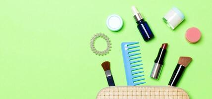 Aerial view of a leather cosmetics bag with make up beauty products spilling out on green background. Beautiful skin concept with copy space photo