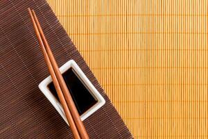 Chopsticks and bowl with soy sauce on two bamboo mat blak and yellow top view with copy space photo