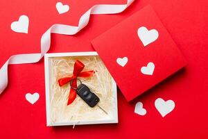 Black car key in a present box with a ribbon and red heart on colored background. Valentine day composition Top view photo