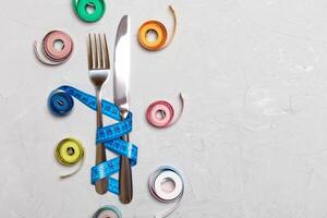 Composition of colored measuring tapes, fork and knife on cement background with empty space for your design. Overweight concept photo