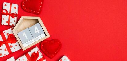 Top view of gift boxes, wooden calendar and red textile hearts on colorful background. The fourteenth of february. St Valentine's day concept with copy space photo