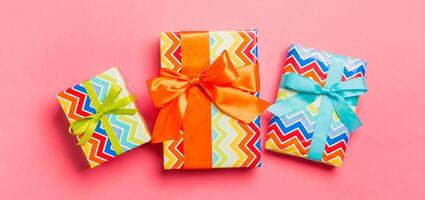 Gift box with blue, green and orange bow for Christmas or New Year day on living coral background, top view photo