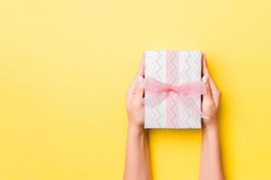 Woman arms holding gift box with colored ribbon on yellow table background, top view and copy space for you design photo