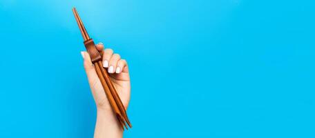 Crop image of female hand holding chopsticks on blue background. Japanese food concept with copy space photo