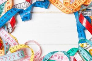 Heap of colorful measuring tapes in the form of frame on wooden background. Top view of slim waist concept with copy space photo
