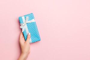 Female's hands holding striped gift box with colored ribbon on living coral background. Christmas concept or other holiday handmade present box, concept top view with copy space photo