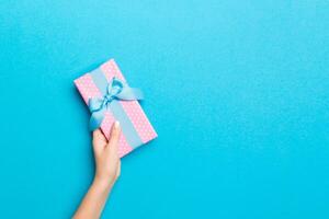 Woman arms holding gift box with colored ribbon on blue table background, top view and copy space for you design photo