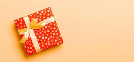 wrapped Christmas or other holiday handmade present in paper with Gold ribbon on orange background. Present box, decoration of gift on colored table, top view with copy space photo