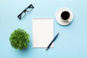 Modern office desk table with notebook and other supplies with cup of coffee. Blank notebook page for you design. Top view, flat lay photo