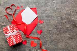 Red paper envelope with empty white card and heart on colored background. top view valentines day concept photo