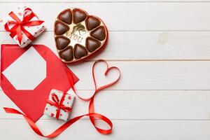 Envelope on colored background for Valentine Day with gift box and chocolate. Heart shaped with gift box of chocolates top view with copy space photo