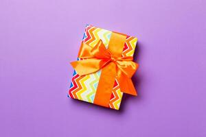 Gift box with orange bow for Christmas or New Year day on purple background, top view with copy space photo