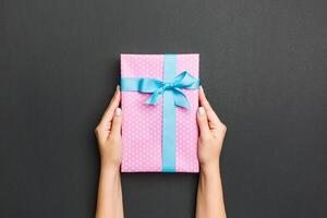 Top view of female hands holding christmas or other holiday handmade present box package in the palms, flat lay on black background with copy space photo