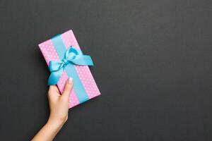 Top view of female hands holding christmas or other holiday handmade present box package in the palms, flat lay on black background with copy space photo