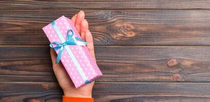 Girl Hands holding craft paper gift box with as a present for Christmas or other holiday on dark wooden background, top view with copy sppace photo