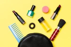 vista superior de los productos de maquillaje caídos de la bolsa de cosméticos sobre fondo amarillo. concepto cosmético con espacio para tu diseño foto