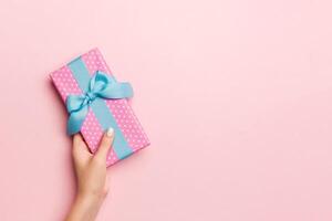 Female's hands holding striped gift box with colored ribbon on living coral background. Christmas concept or other holiday handmade present box, concept top view with copy space photo