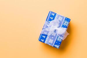 envuelto Navidad o otro fiesta hecho a mano presente en papel con blanco cinta en naranja antecedentes. presente caja, decoración de regalo en de colores mesa, parte superior ver con Copiar espacio foto