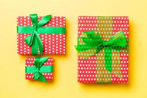 wrapped Christmas or other holiday handmade present in paper with green ribbon on yellow background. Present box, decoration of gift on colored table, top view photo