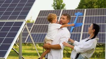 familj med sol- paneler, förnybar energi begrepp. föräldrar och bebis son spelar tillsammans med leksak plan nära sol- paneler video